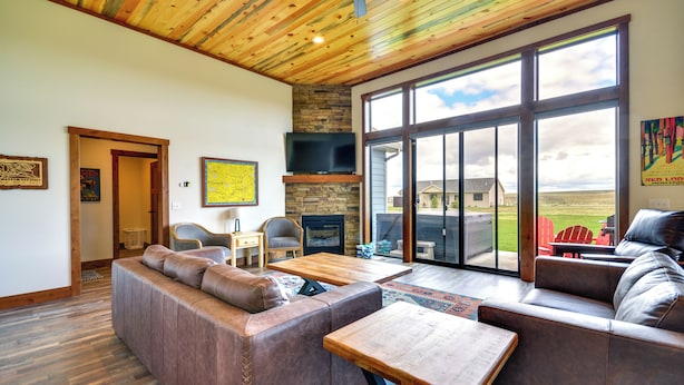 Un salón amplio con un gran ventanal, chimenea de piedra y sofás de cuero.