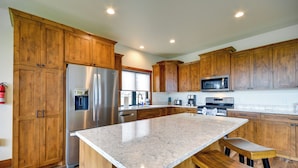 Cocina con armarios de madera, electrodomésticos de acero inoxidable y encimera de mármol.