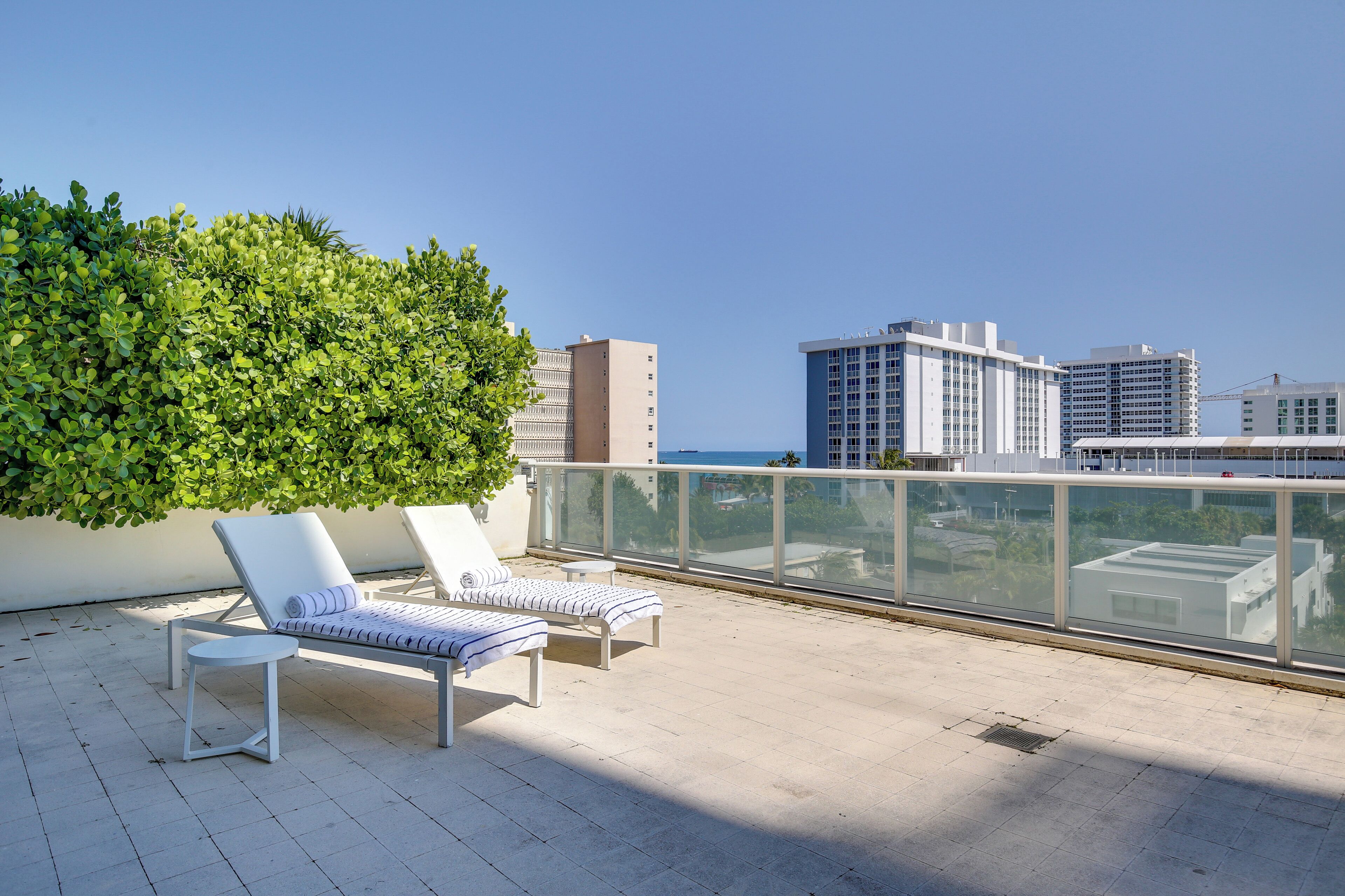 Una terraza en la azotea con dos sillones blancos, una mesita y un seto verde grande.