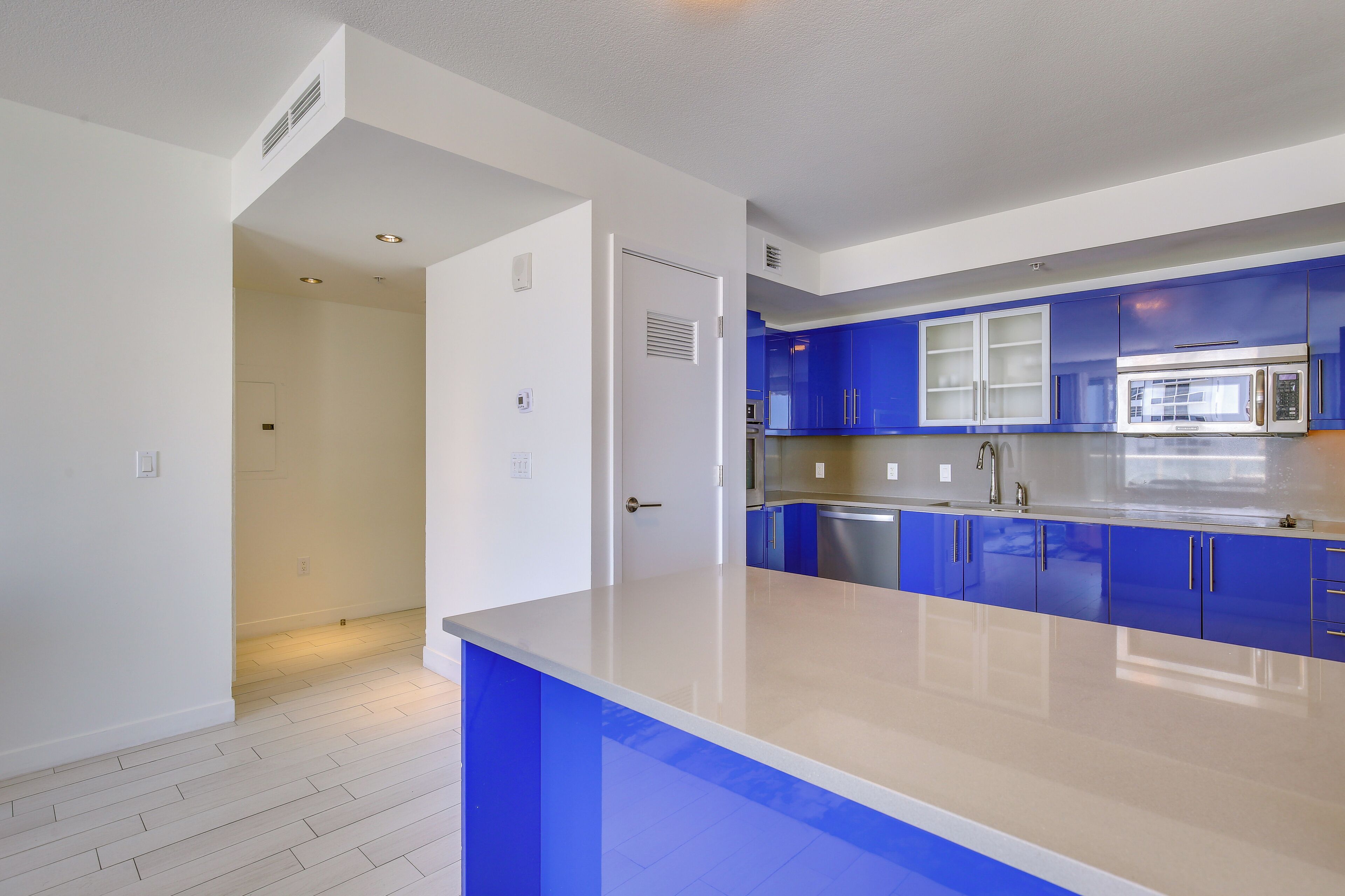 Una cocina moderna con armarios azules, un microondas de acero inoxidable y una encimera blanca.