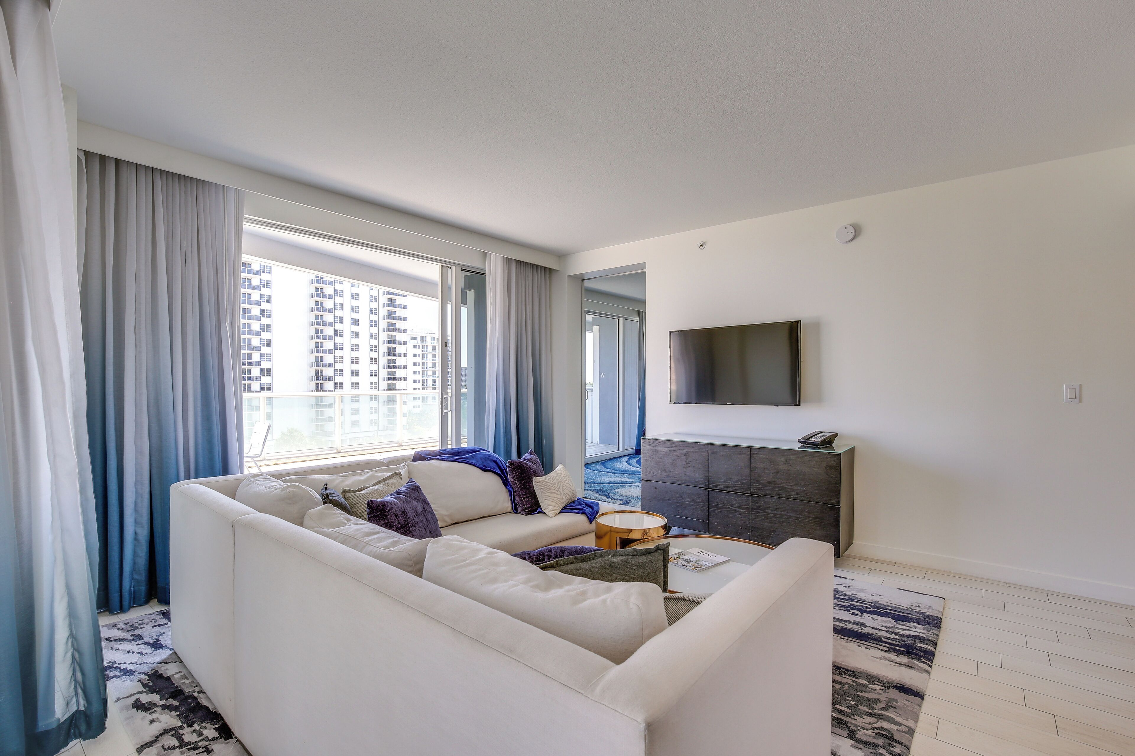 A modern living room with a white sofa, a coffee table, and a TV mounted on the wall.