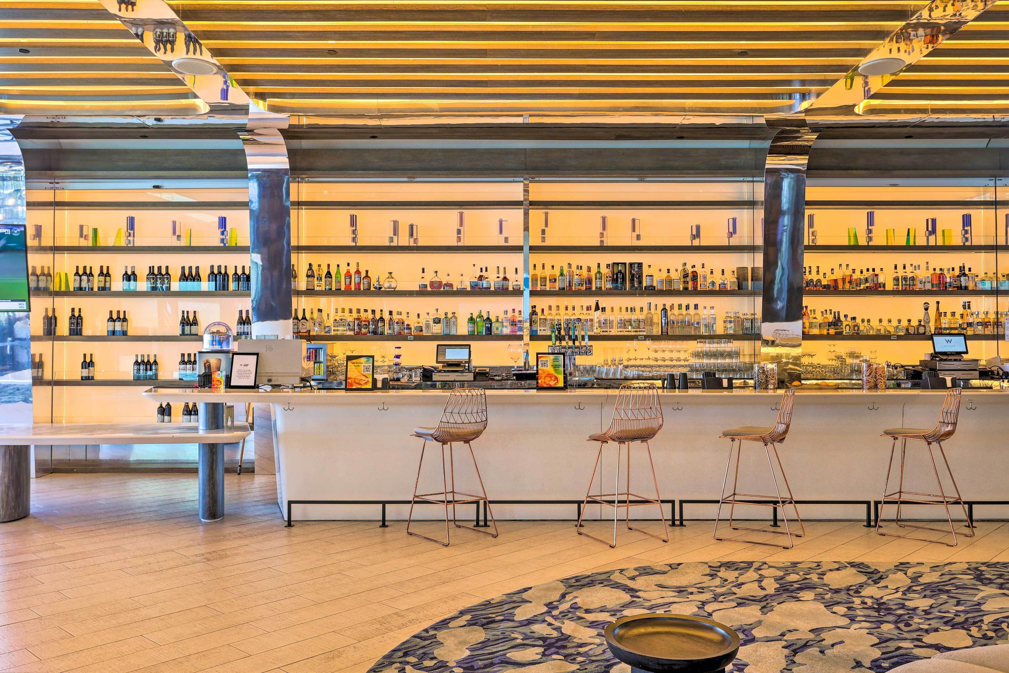 Un espace bar doté d’un long comptoir, de plusieurs étagères remplies de bouteilles et de deux tabourets de bar.