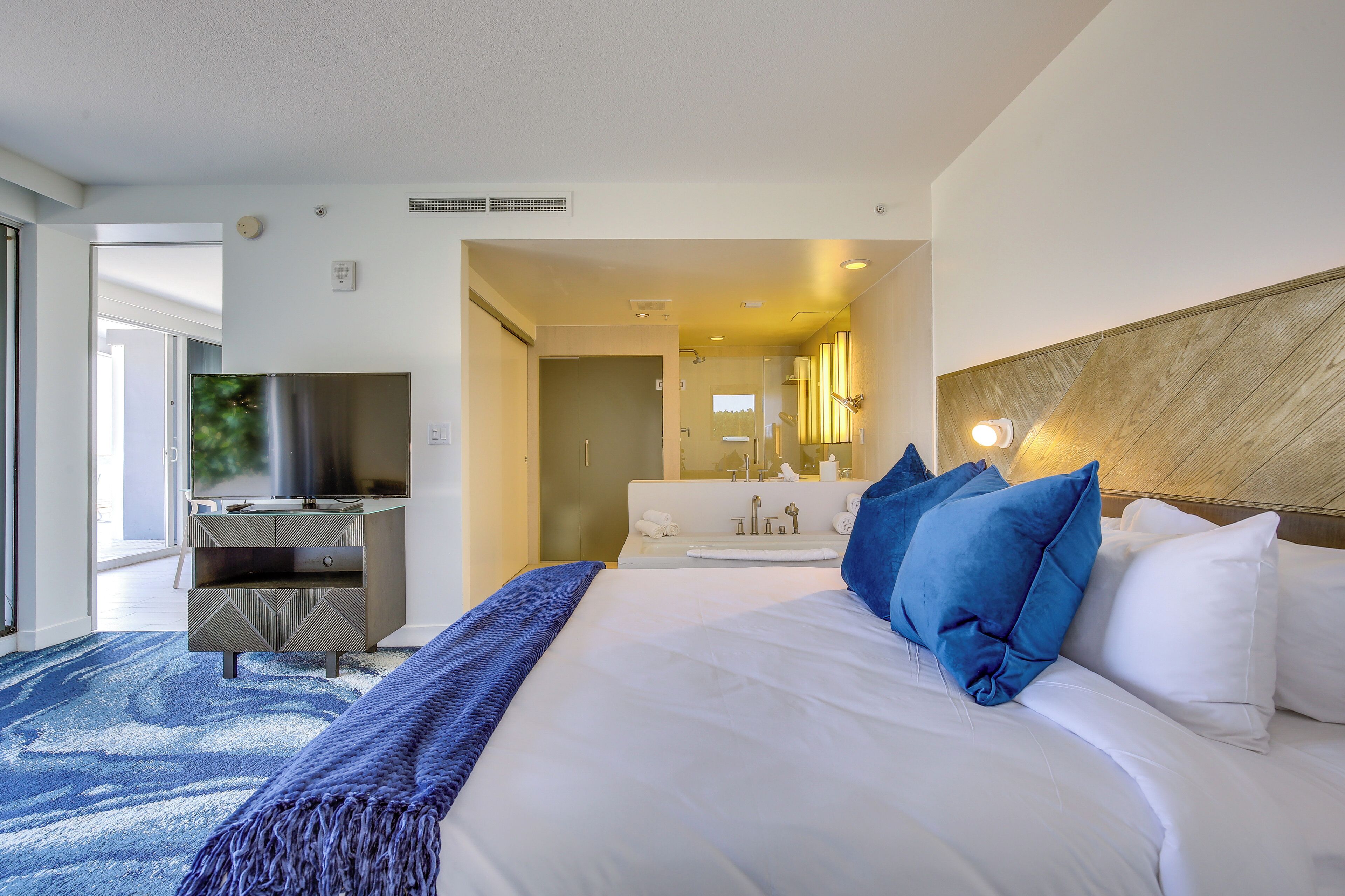 A hotel room with a large bed, a television, a bathroom with a mirror, and a view of the outdoors.