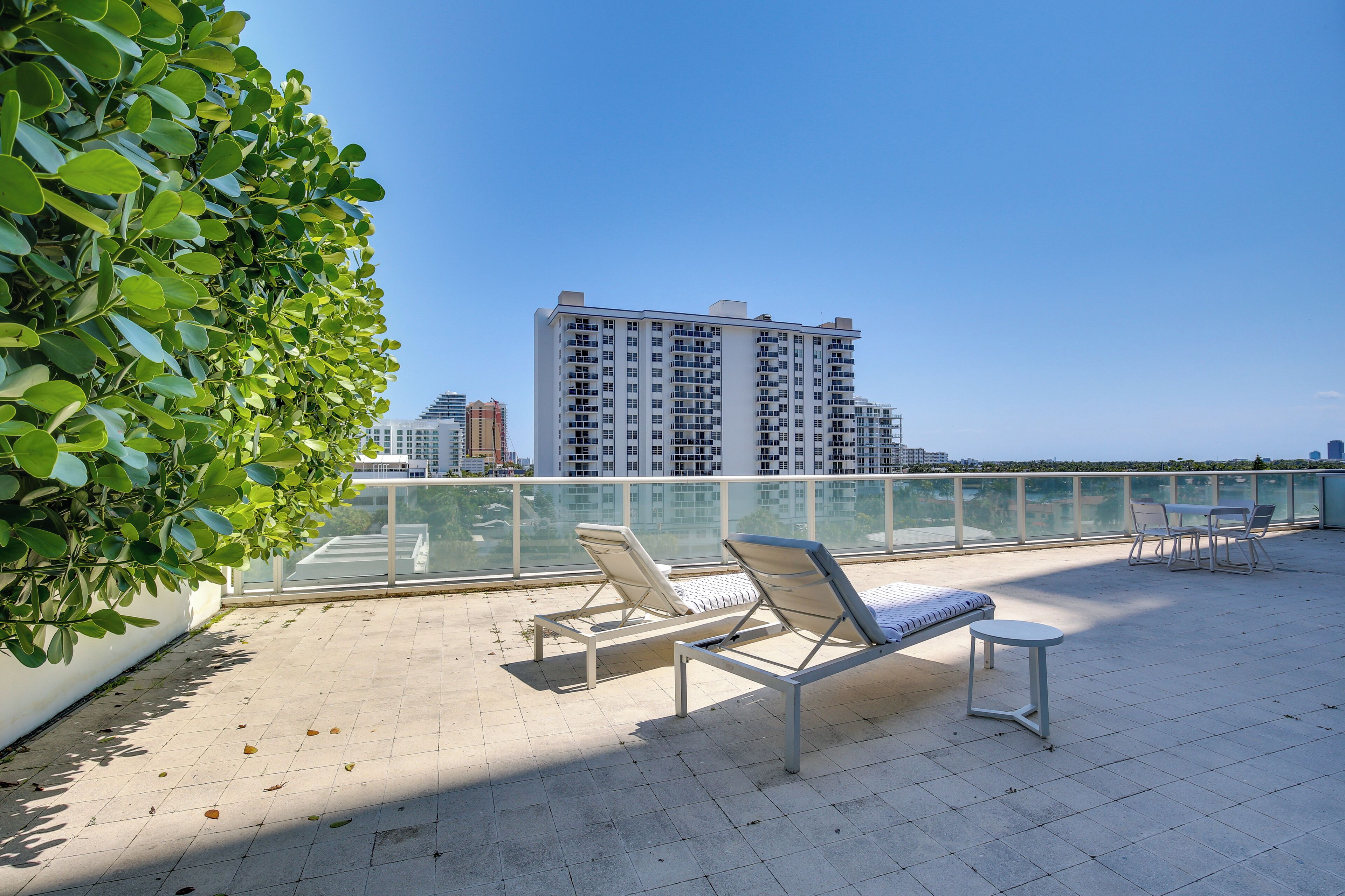 A rooftop terrace with lounge chairs and a small table, overlooking a cityscape and water.