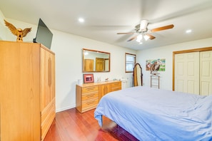 Une chambre à coucher comprenant un lit, une armoire en bois, une commode, un miroir, un ventilateur de plafond et une porte.