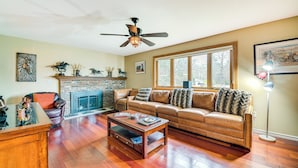 A living room with a leather sofa, a coffee table, a fireplace, and a ceiling fan. - Saratoga Springs Home Near Skidmore College! (Saratoga Springs)