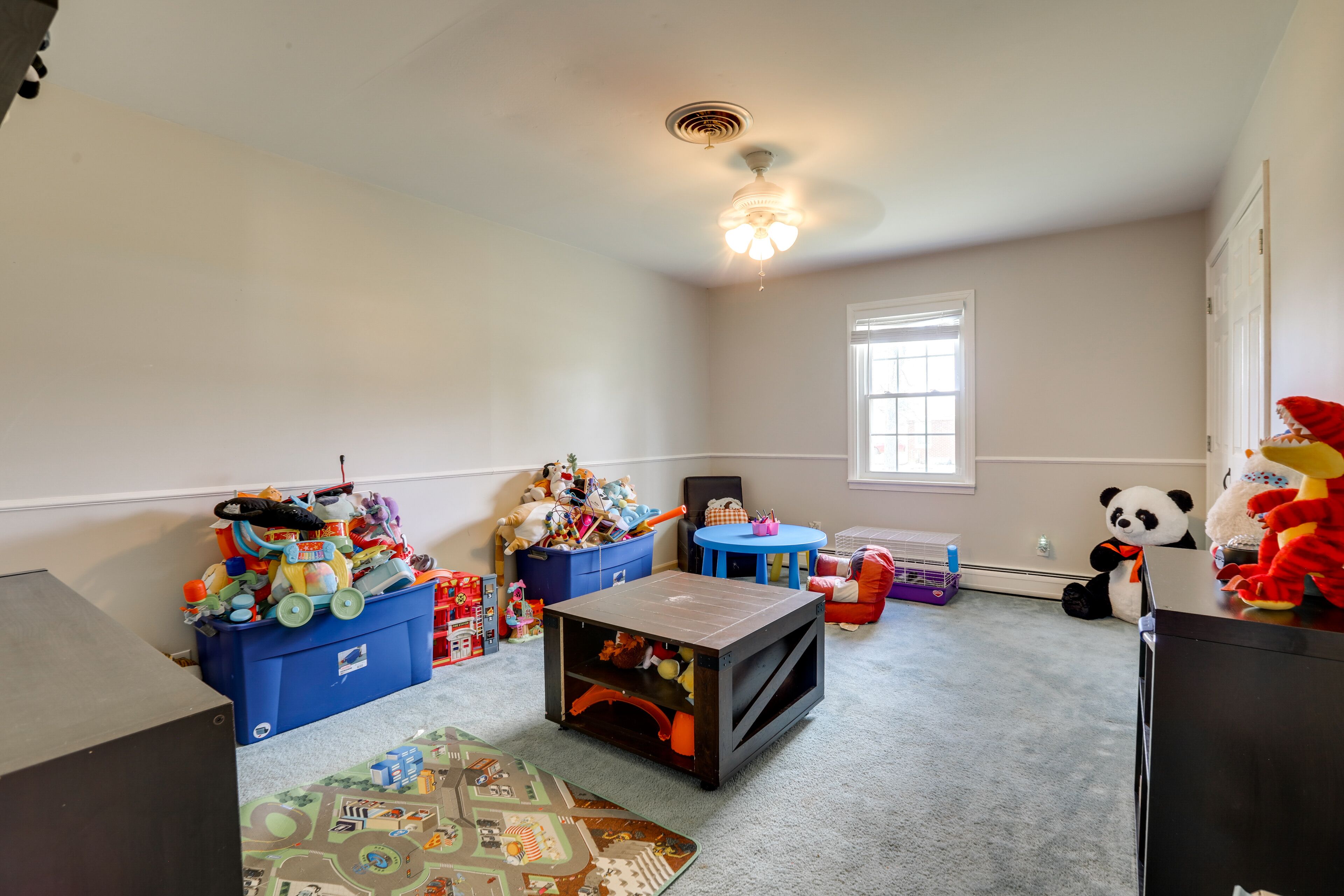 A child's playroom with toys, a ceiling fan, and a window.