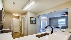 Une cuisine moderne avec des plans de travail blancs, un évier en acier inoxydable et un ventilateur de plafond.
