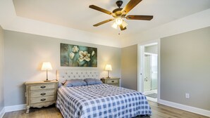 Une chambre à coucher avec un lit, deux tables de chevet, un ventilateur de plafond et un tableau au mur.