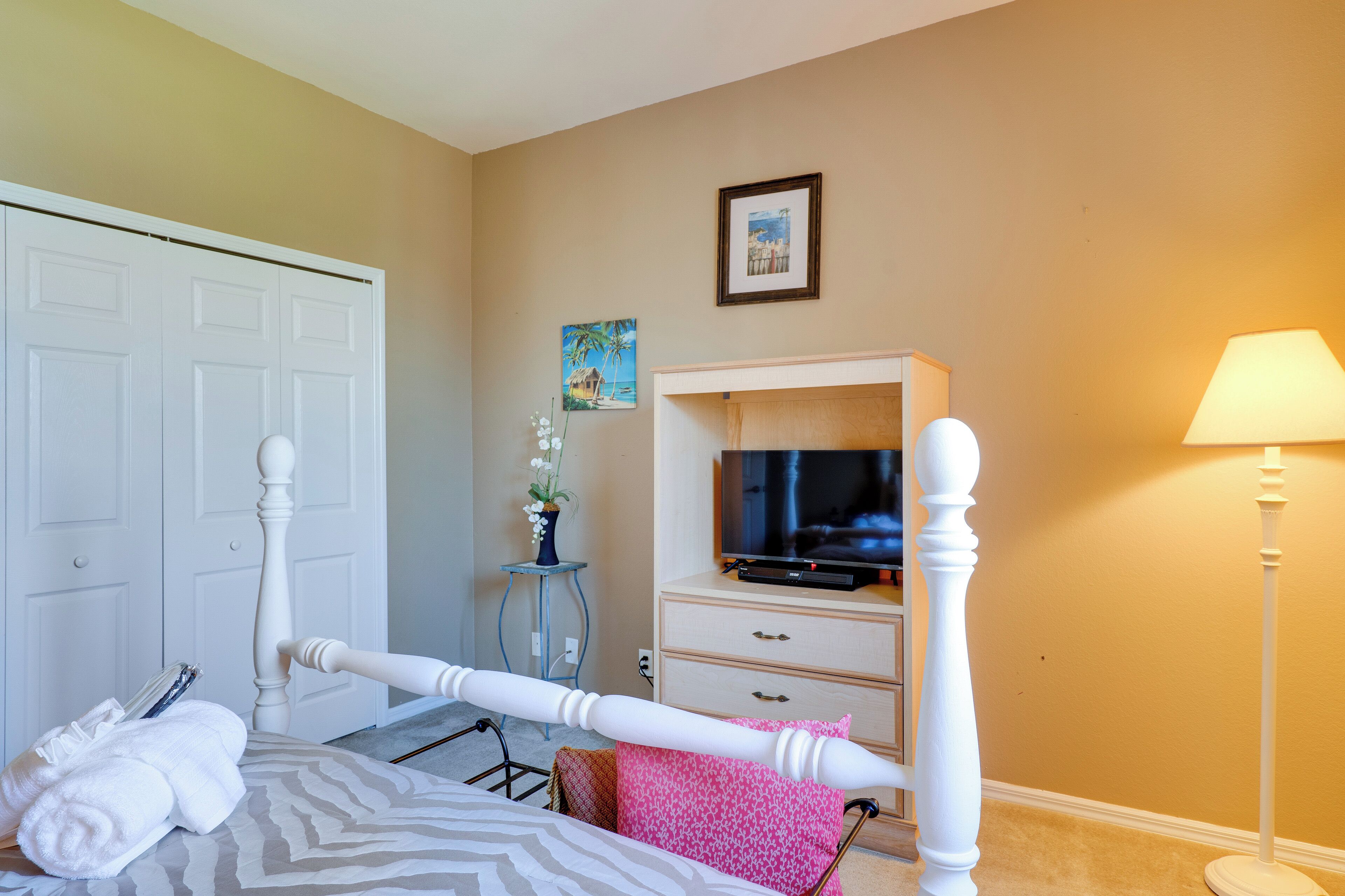 A bedroom with a bed, a television on a stand, a lamp, a dresser, and a door.
