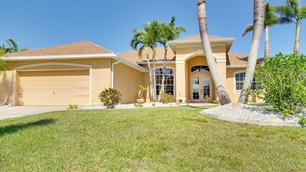 A two-story house with a garage, palm trees, and a well-maintained lawn. - Near Sand & Sun, Cape Coral Home w/ Private Pool (Cape Coral)