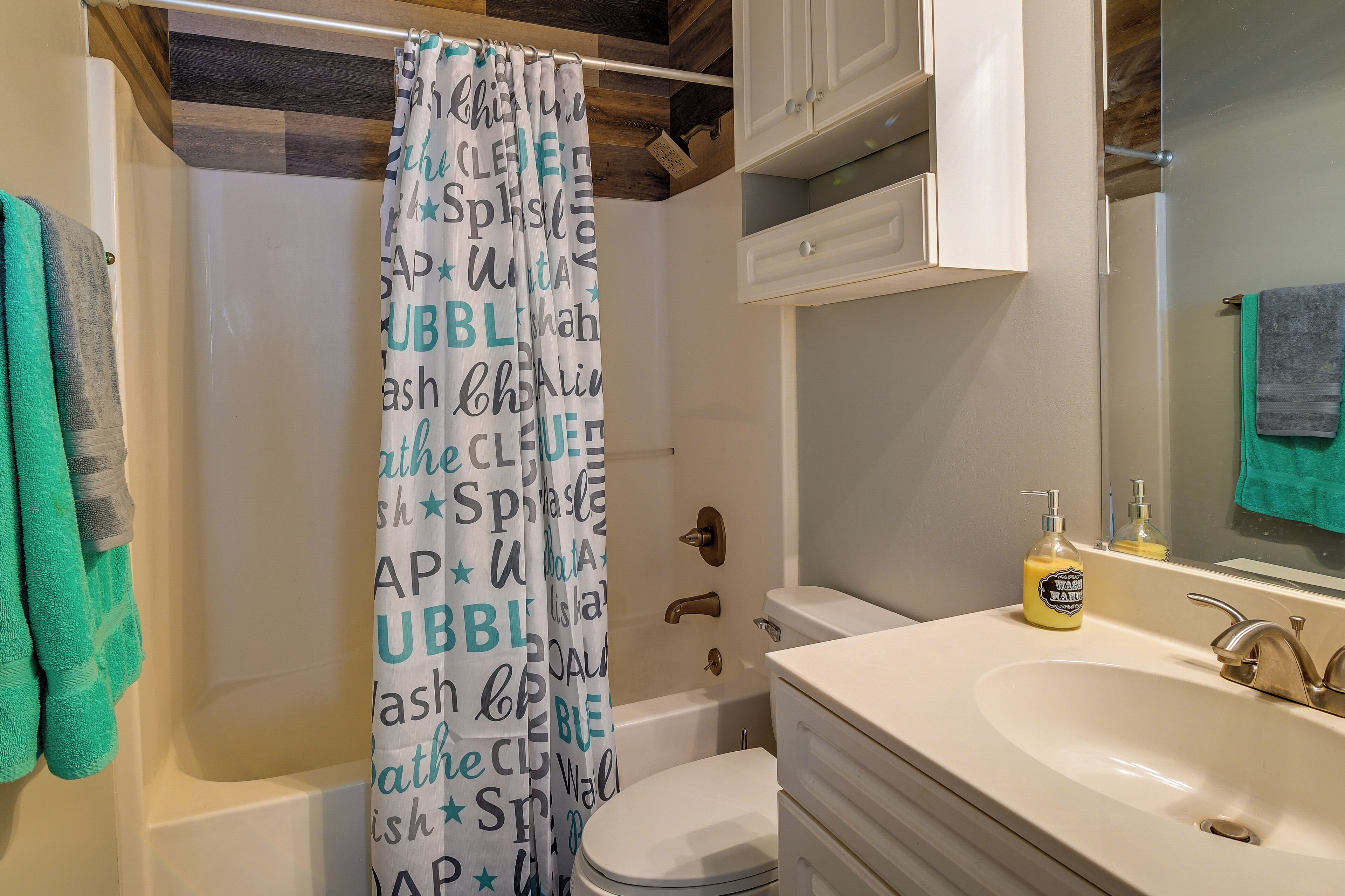 A bathroom with a shower curtain, toilet, sink, and cabinets.