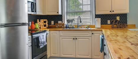 A kitchen with white cabinets, a stainless steel refrigerator, a microwave, and a wooden countertop.