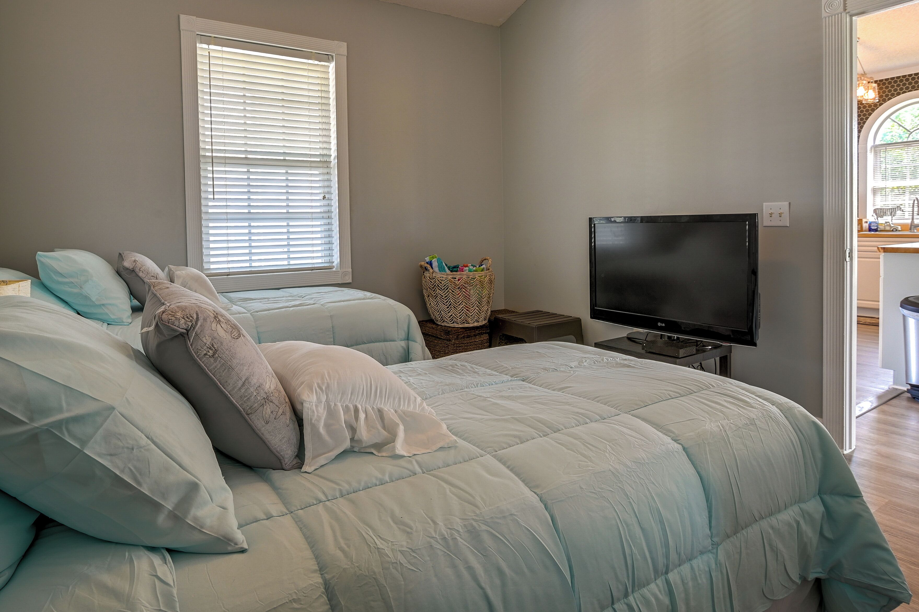 A bedroom with two beds, a TV, and a window with blinds.