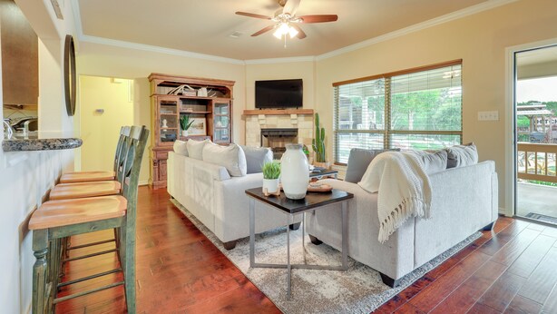 A spacious living room with a fireplace, a ceiling fan, and a large window with blinds. - New Braunfels Home w/ Pool 2 Mi to Guadalupe River (New Braunfels)