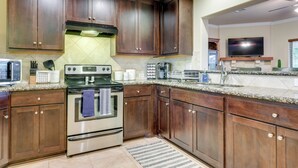 A kitchen with dark wooden cabinets, stainless steel appliances, a granite countertop, and a flat-screen TV above the sink. - New Braunfels Home w/ Pool 2 Mi to Guadalupe River (New Braunfels)