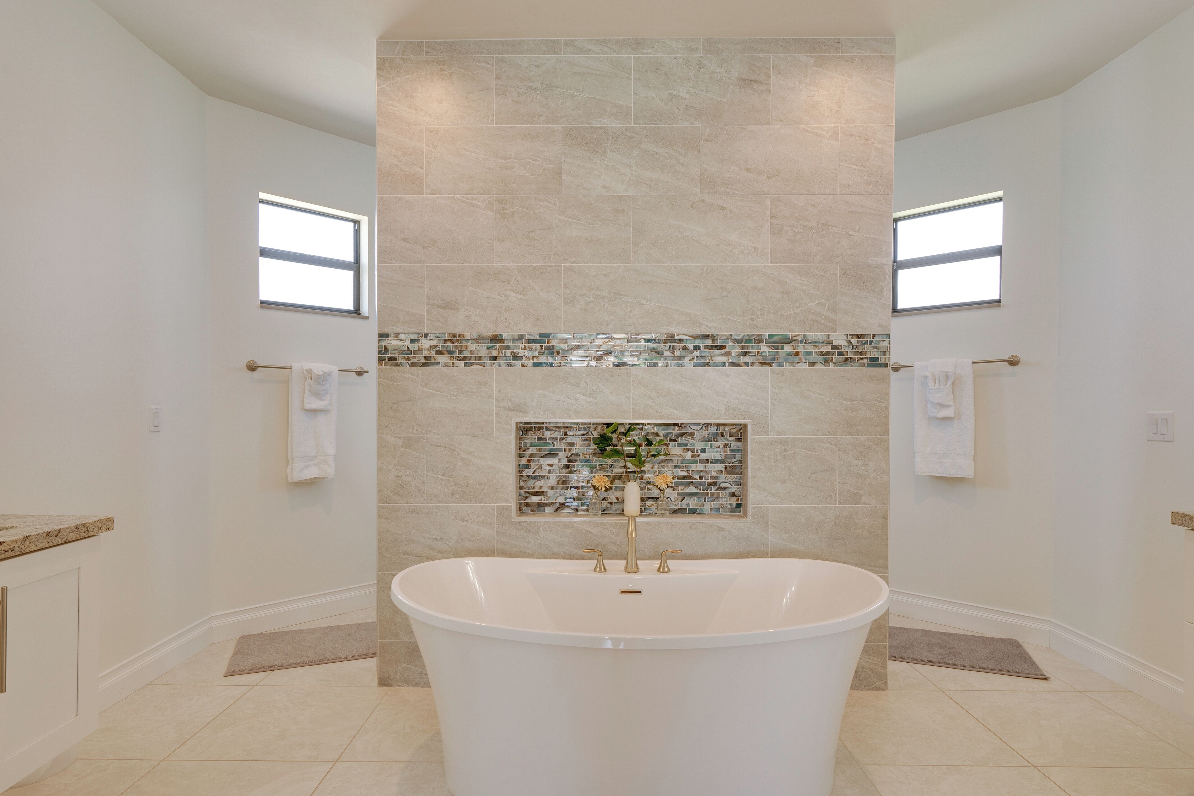 Un baño moderno con una bañera independiente, un salpicadero de mosaico y dos ventanas que ofrecen luz natural.