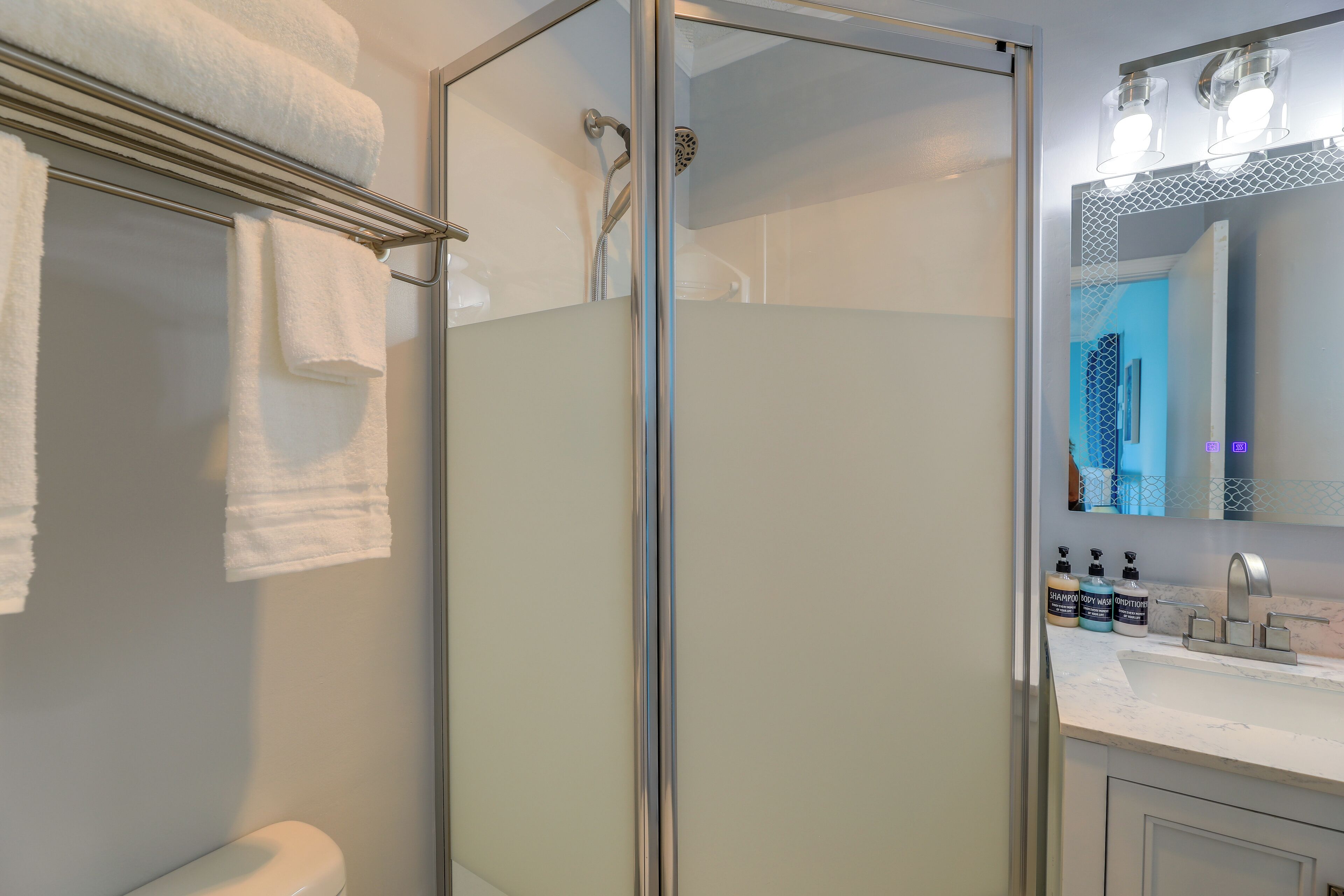 A modern bathroom with a glass-enclosed shower, a toilet, and a vanity with a mirror and sink.
