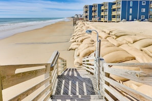 A wooden boardwalk leading to a beach with sandbags for protection, overlooking the ocean and a row of blue buildings with balconies. - Family Beach Retreat in N Topsail: Steps to Shore! (Sneads Ferry)