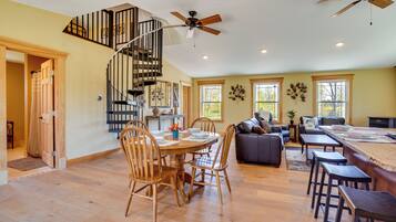 A spacious living area with a dining table, chairs, a sofa, and a kitchen area with a spiral staircase.