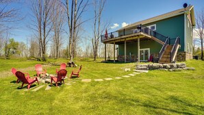 A green house with a covered porch, a staircase, and a fire pit with chairs.