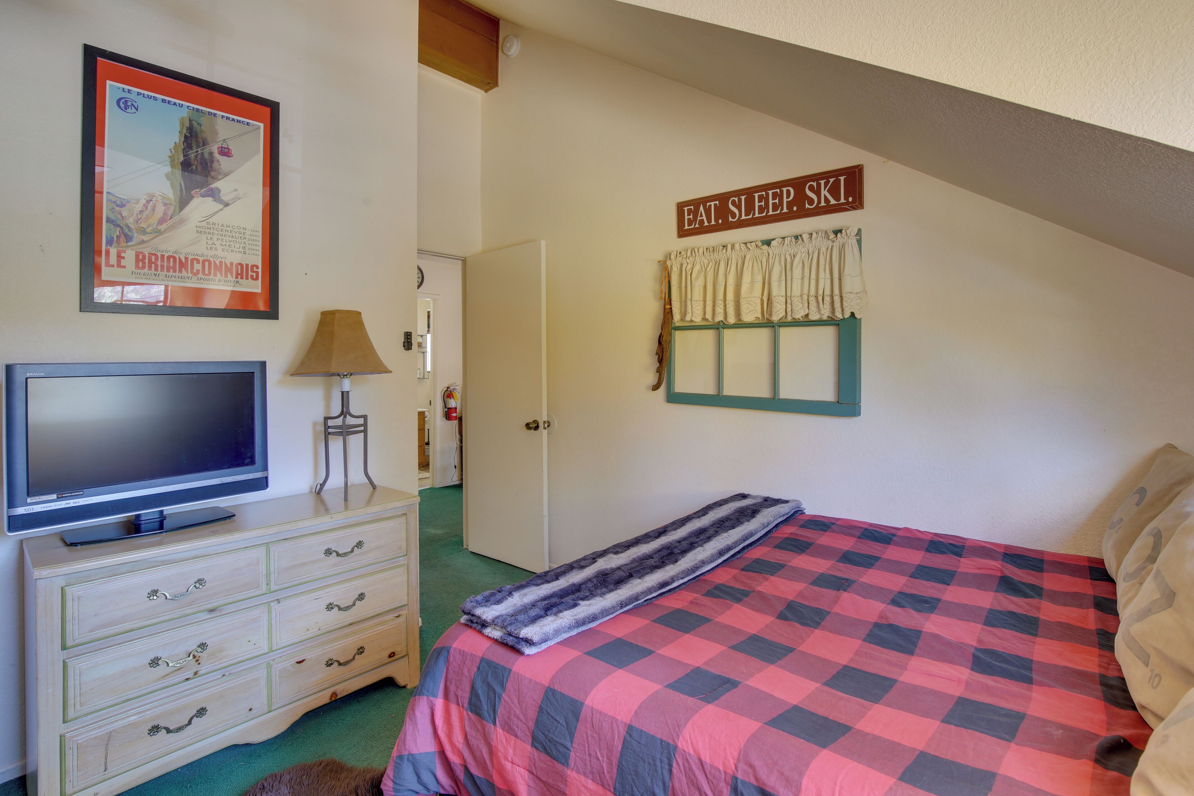 Ein Schlafzimmer mit einem Bett, einem Fernseher auf einer Kommode, einem Schild mit der Aufschrift "EAT. SLEEP. SKI." und einem Poster an der Wand.