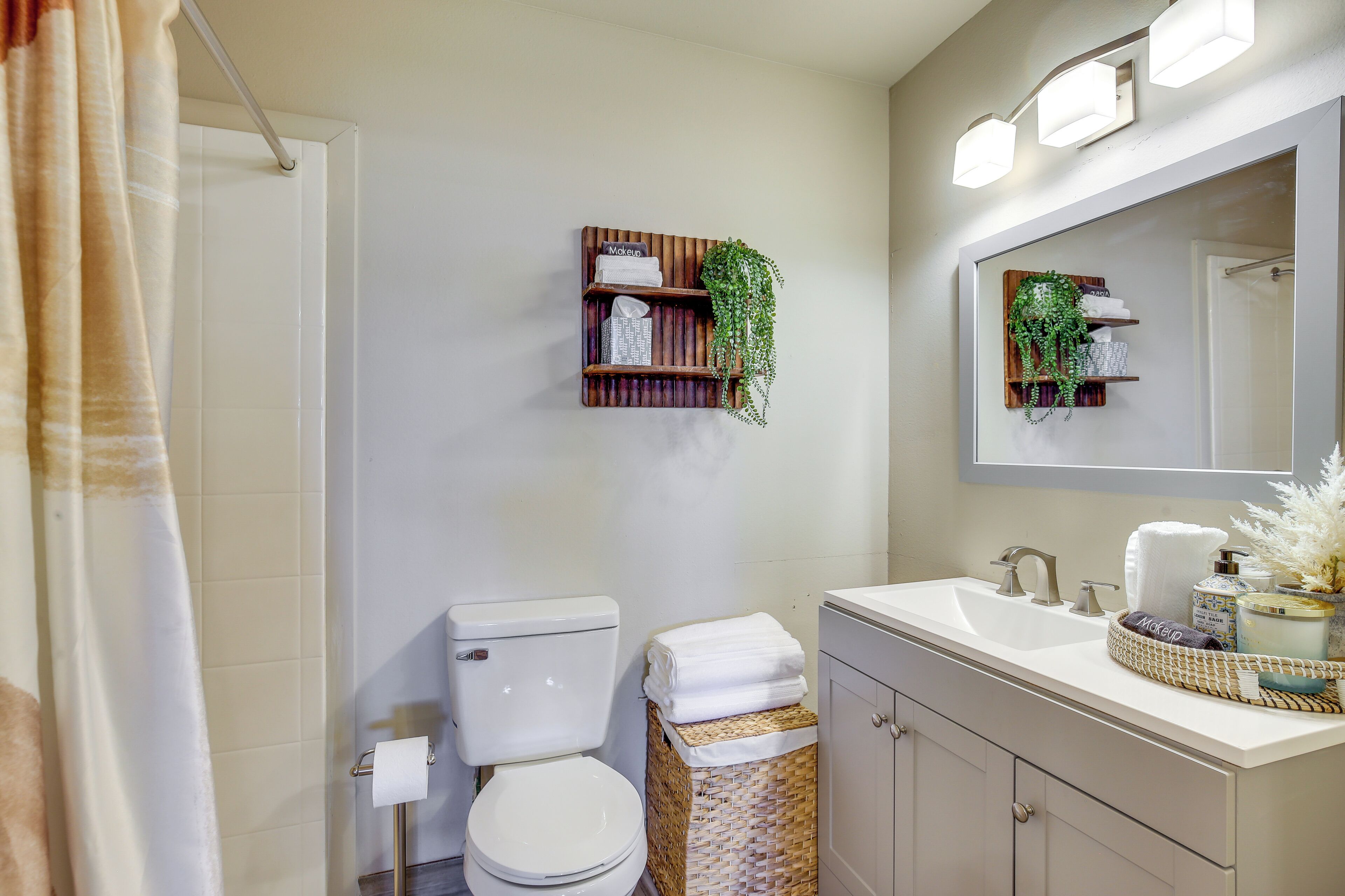 A bathroom with a toilet, sink, and mirror. There is a shelf with plants and toiletries.