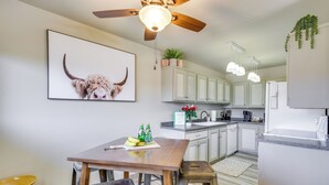 Une cuisine moderne avec des meubles blancs, une table à manger en bois et un ventilateur de plafond.