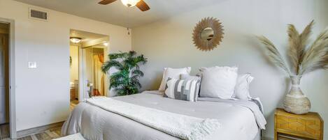 A bedroom with a bed, a ceiling fan, a bedside table with a vase, and a wall-mounted mirror.