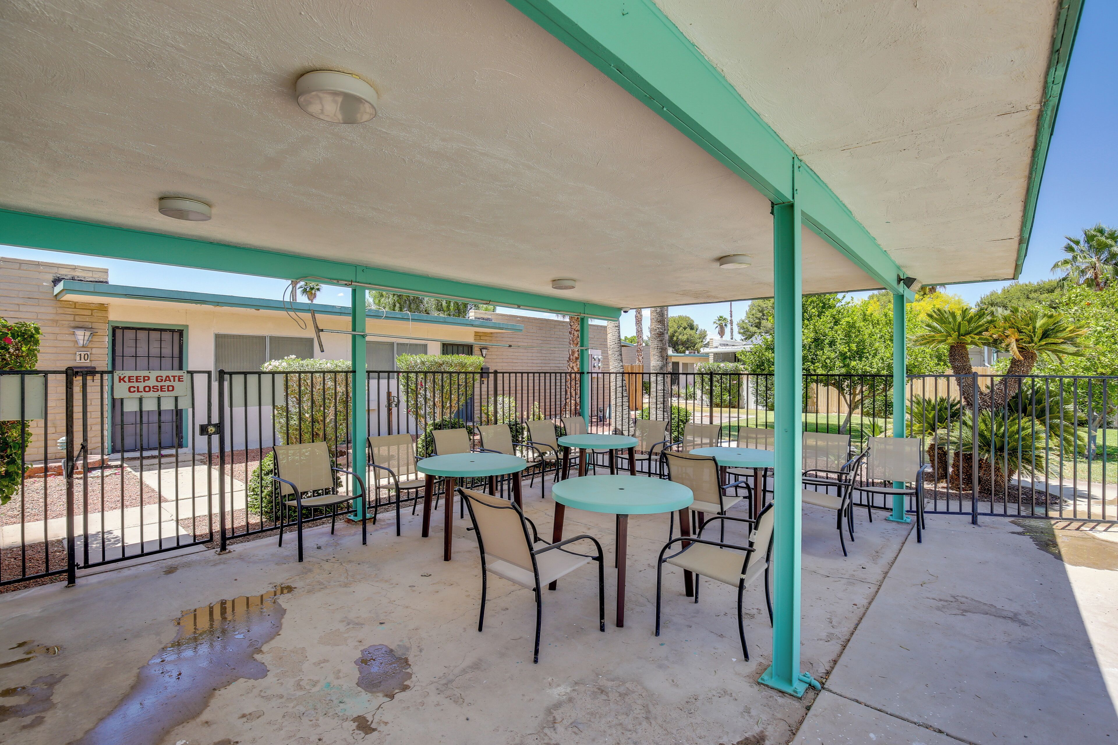 An outdoor patio area with tables and chairs, a closed gate, and a building in the background.