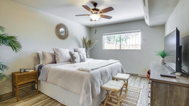 Une chambre à coucher avec un lit, des tables de chevet, un ventilateur de plafond, une télévision et une fenêtre.