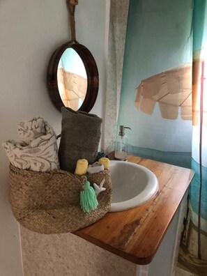 Un baño con tocador de madera, un lavabo blanco, un espejo y una cesta de mimbre con toallas y un borlón verde.