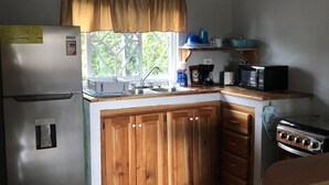 A compact kitchen with a refrigerator, stove, microwave, and wooden cabinets. - Seacret Studios - Cozy Jamaican Retreat Apts by RedAwning (Negril)