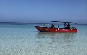 Una pequeña embarcación roja con el nombre "Coca Cola" en el costado, flotando sobre agua tranquila y cristalina.