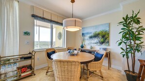 Un coin repas avec des chaises en osier, une table ronde, un luminaire suspendu, une fenêtre donnant sur un beau paysage et une plante en pot.