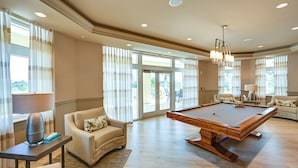 Un salon spacieux doté d’une table de billard, de sièges confortables et de grandes fenêtres offrant une vue sur l’extérieur.