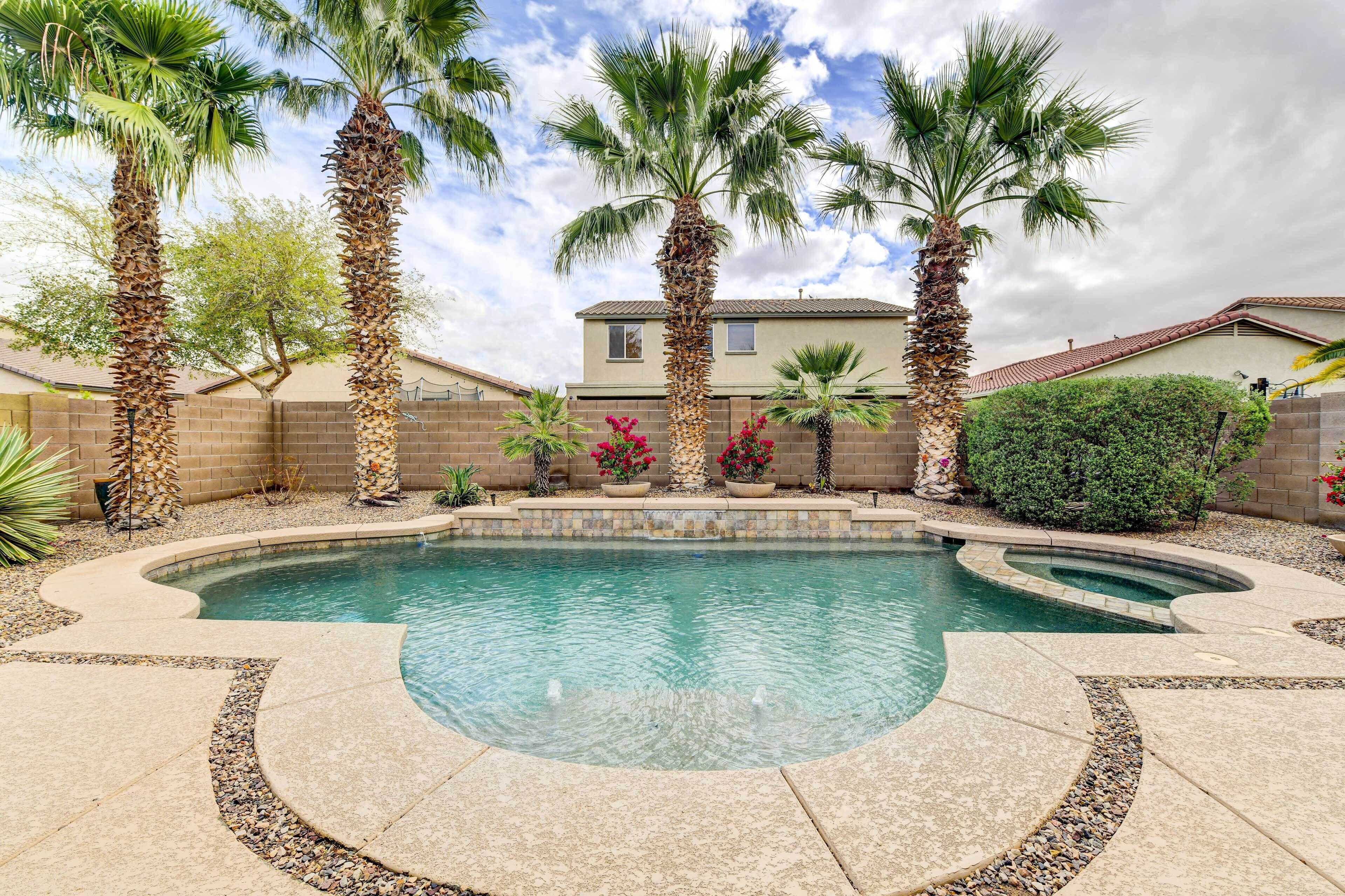 A swimming pool with a curved design, surrounded by palm trees and a brick wall.