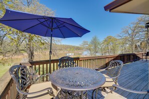 A deck with a round table and chairs, a blue umbrella, and a view of a lake. - Spacious Vacation Rental Home on Eufaula Lake! (Eufaula)
