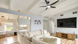 A modern living room with a large sectional sofa, a flat-screen TV, and a ceiling fan. - Riverfront Elkhart Rental: Deck & Ping Pong Table! (Elkhart)