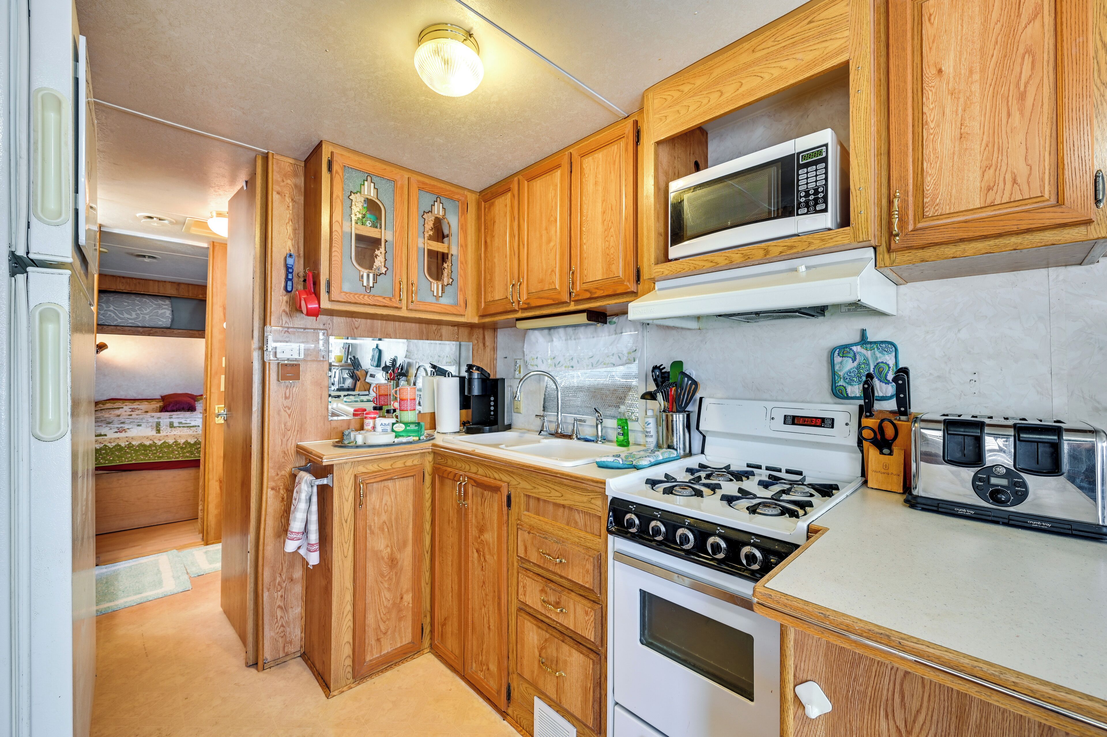 A compact kitchen with wooden cabinets, a microwave, a stove, and a toaster.