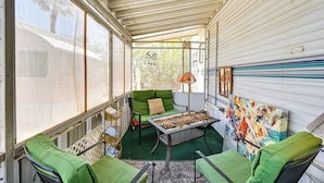 Ein überdachter Patio-Bereich mit einem grünen Sofa, einem Metalltisch und einem farbenfrohen Gemälde an der Wand.