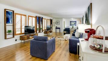 Uma sala de estar ampla com uma televisão grande, piso de madeira e um sofá azul.