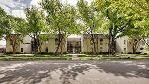 Un edificio a due piani con un ingresso centrale, circondato da alberi e un vialetto lastricato.