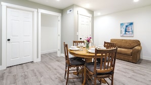 A dining area with a wooden table set for four, surrounded by chairs with cushions. There is a brown sofa against the wall and a white door to the left. - Orem Vacation Rental Apartment Near BYU Campus! (Orem)