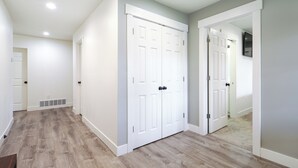 A hallway with a wooden floor, white walls, and a white door with a vent. - Orem Vacation Rental Apartment Near BYU Campus! (Orem)