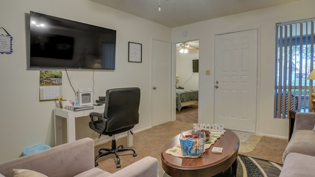 A living room with a flat-screen TV, a desk with a computer, a chair, and a coffee table with snacks. - Peaceful Peoria Vacation Rental: Near Westgate! (Peoria)