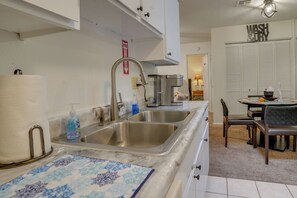 A kitchen with a stainless steel sink, a paper towel holder, and a dish soap dispenser. There is a sign indicating a fire exit and a 'WASH & DRY' sign above a white cabinet.