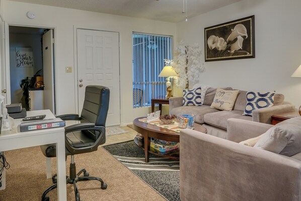 A living room with a desk, office chair, couch, and a decorative plant.