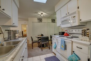 A compact kitchen with white cabinets, a stove, microwave, and a sink.
