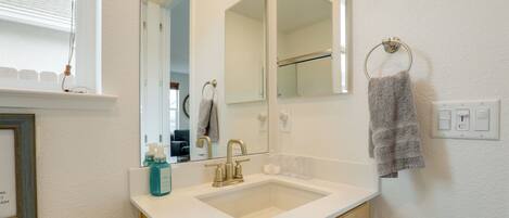 A bathroom with a white sink, a mirror, a towel ring, and a framed picture on the wall.